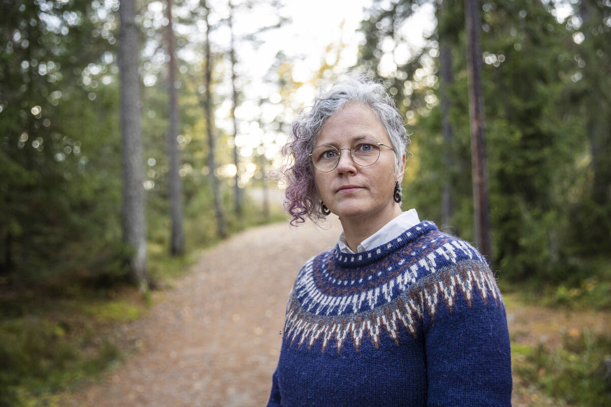 Kvinna i blå tröja står i en skogsbacke