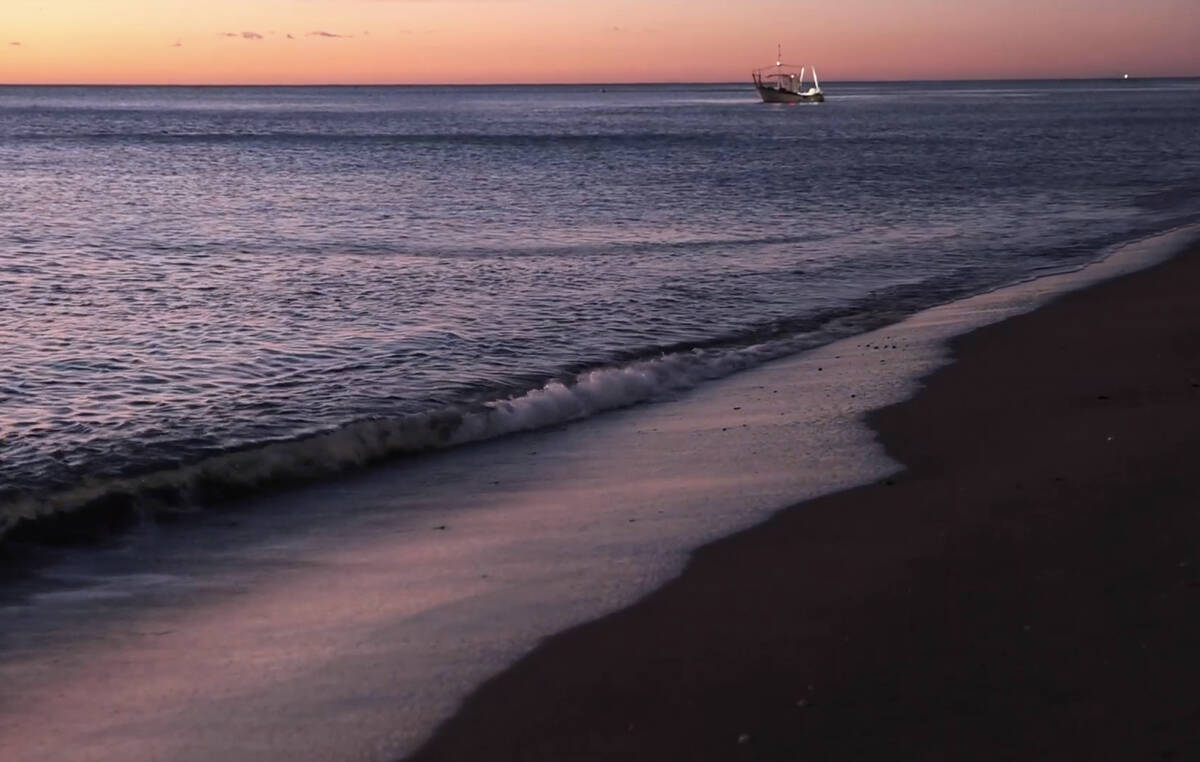 Strand vid Medelhavet i soluppgång. I fjärran syns en fiskebåt.