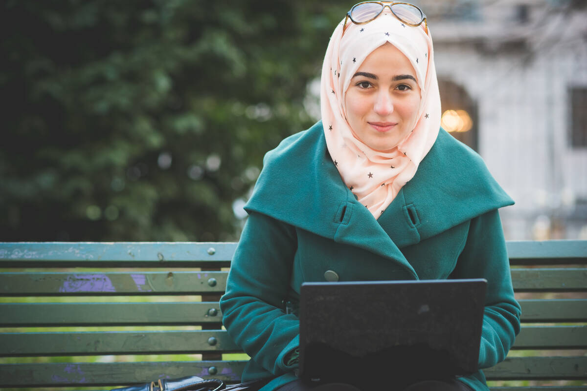 Kvinna med laptop sitter på en parkbänk.