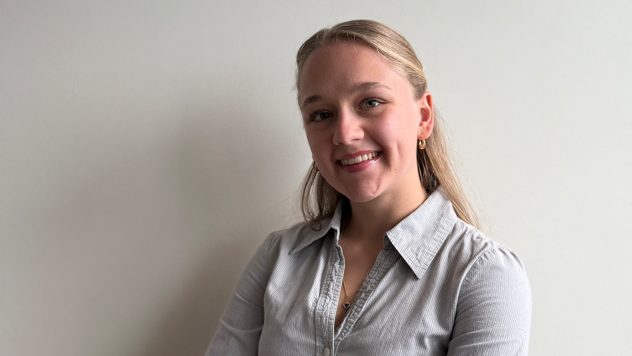 En kvinna med blont hår och skjorta ler in i kameran